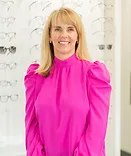 Woman with blonde hair wearing bright pink blouse smiling at camera in professional office setting.