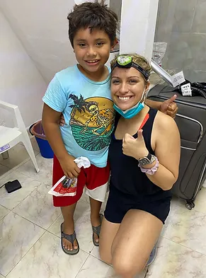 Two young people smiling together in a bathroom, wearing casual summer clothing and holding water bottles.