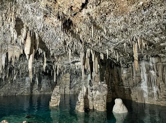 Underground cave with stalactites hanging above turquoise water and limestone formations.