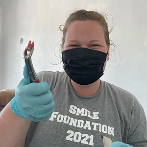 Healthcare worker wearing mask and gloves holds up syringe, promoting Smile Foundation 2021.