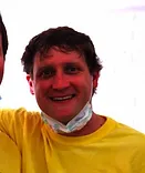 Man in yellow shirt smiling at camera, wearing face paint, indoors.