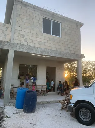 People gathered on porch of concrete house during evening, supporting community development project.