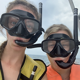 Two people wearing snorkeling masks and life jackets smile at the camera outdoors near water.