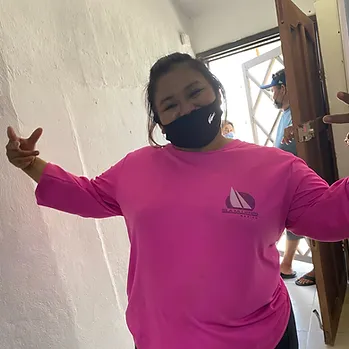 Woman wearing pink Smile Foundation shirt with arms outstretched, smiling indoors.