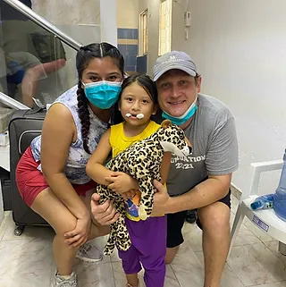 Family holding spotted leopard cub indoors, wearing masks, smiling at camera.